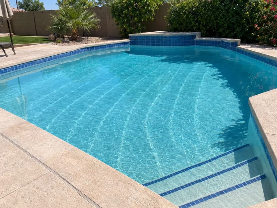 A clean backyard pool with blue tile and steps on a sunny afternoon